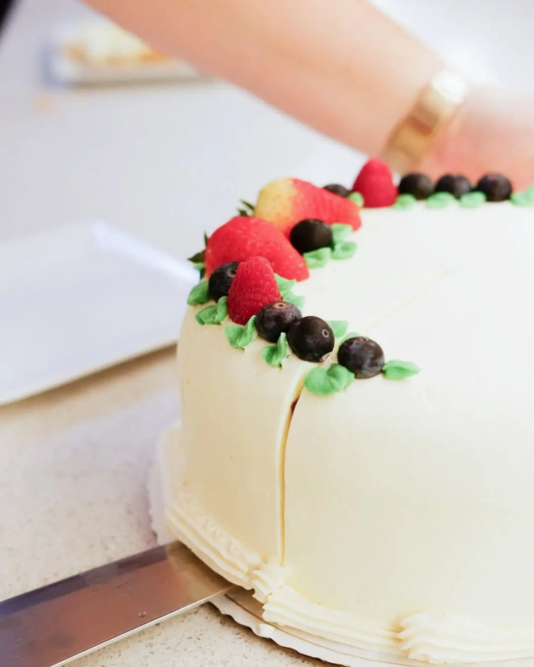Berry Patch cake topped with fresh berries being sliced