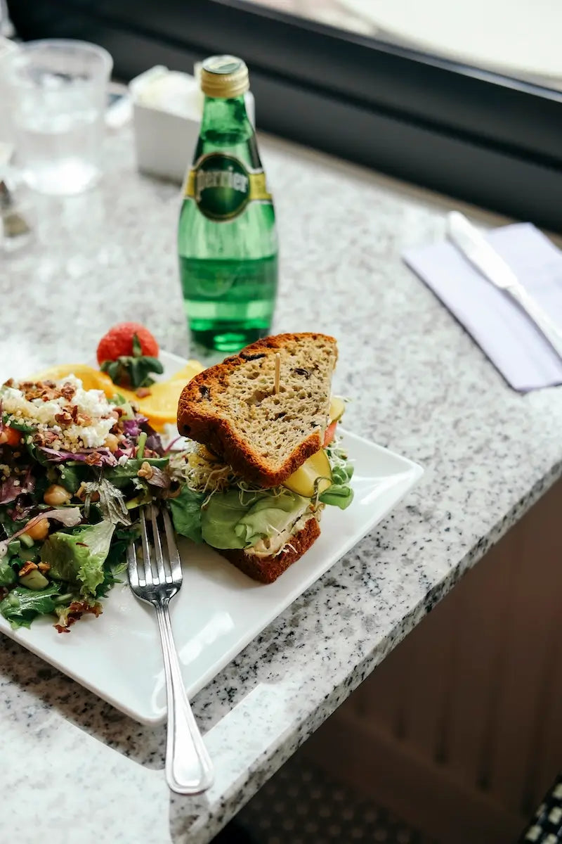 Gluten-free veggie sandwich on seeded bread, served with a mixed green salad topped with feta and chickpeas.