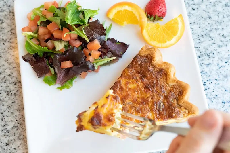 A slice of gluten-free quiche served with a mixed greens side salad.