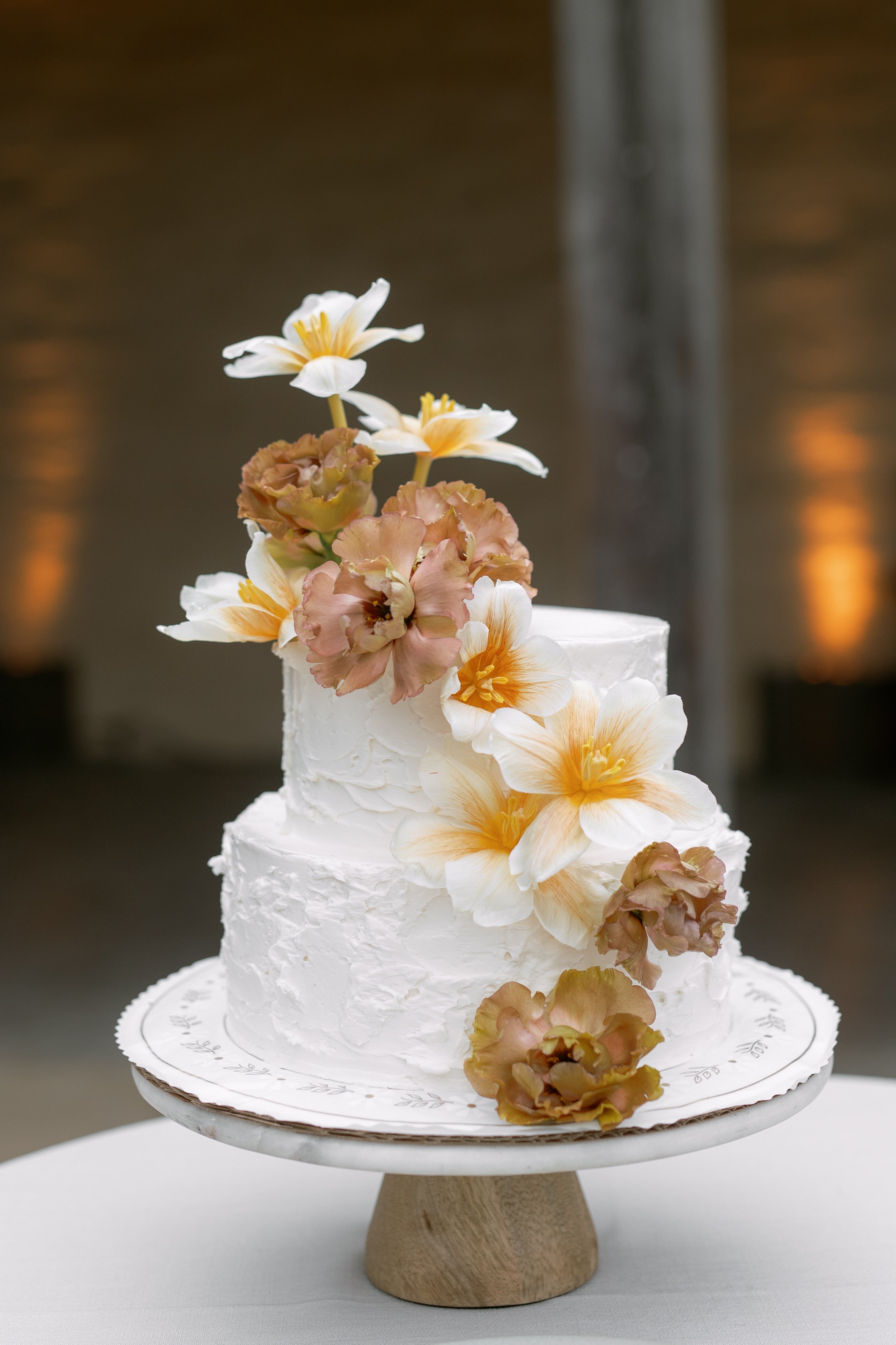 Two-tiered white wedding cake with floral decorations on a wooden stand.