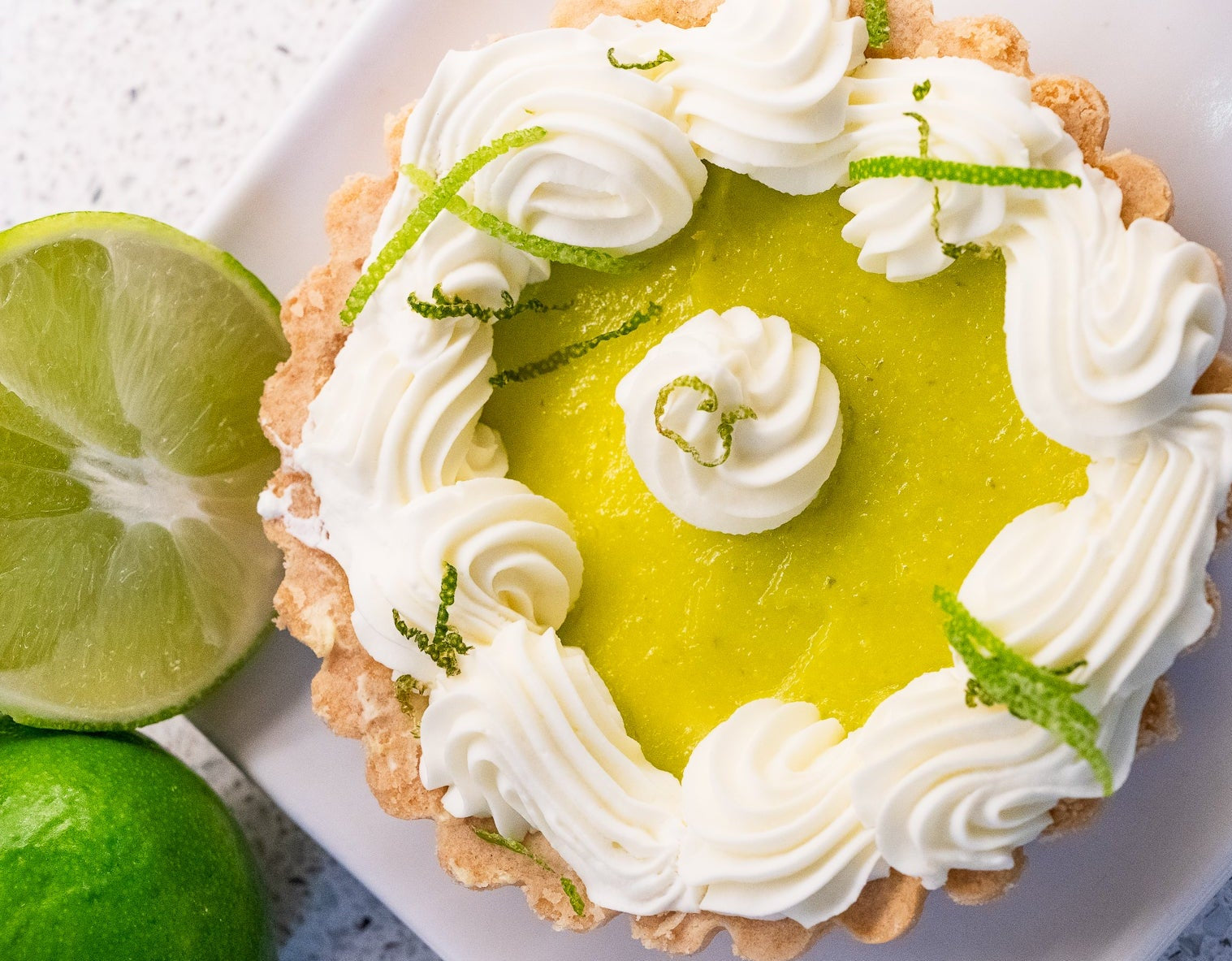 Key lime pie with whipped cream and lime zest on a white plate