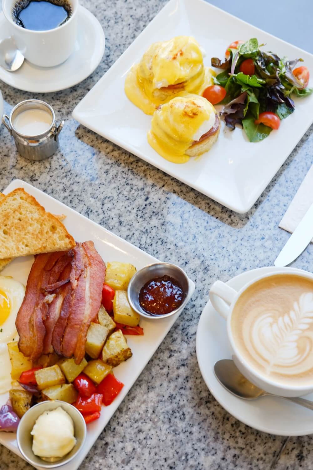 A full breakfast featuring eggs benedict, bacon, breakfast potatoes, and a latte, prepared in a dedicated gluten-free kitchen.