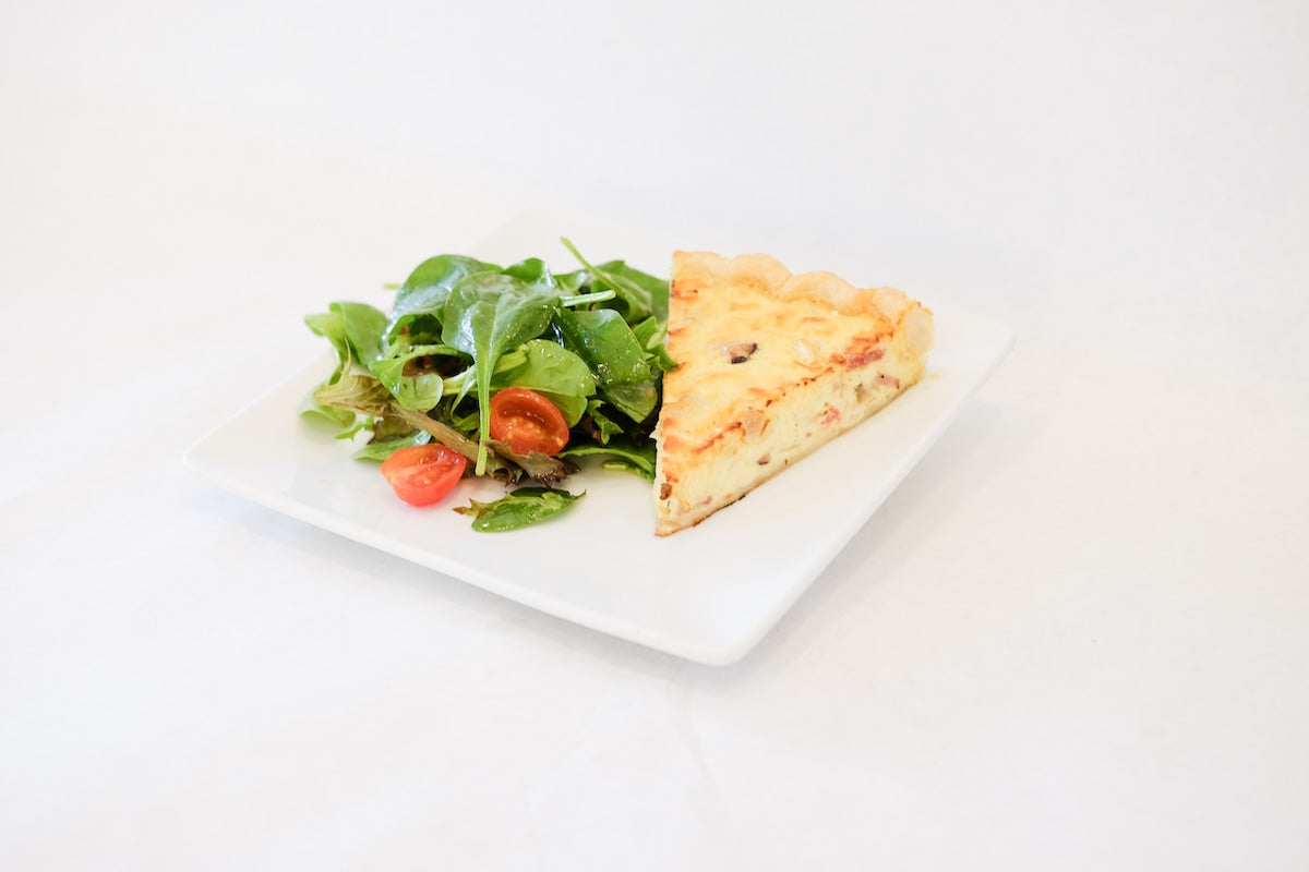 A slice of freshly baked quiche served with a side of mixed greens and cherry tomatoes for lunch.
