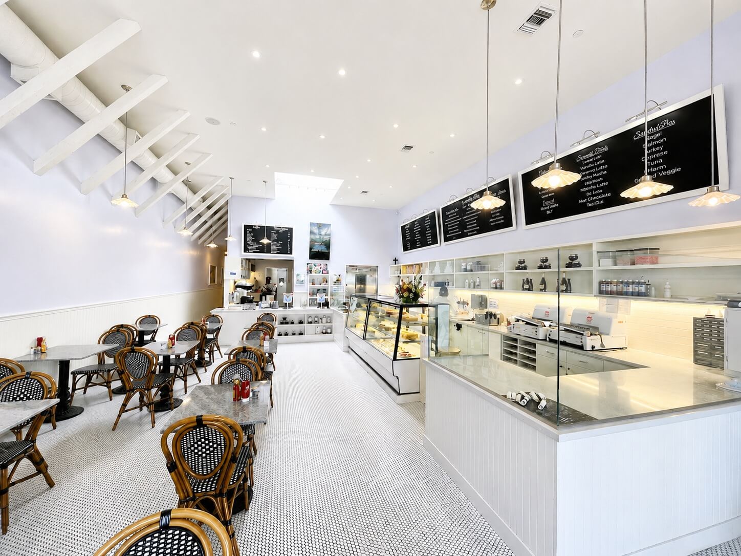 The bright and elegant interior of Lilac Pâtisserie in Santa Barbara, featuring marble tables and woven bistro chairs for private events.