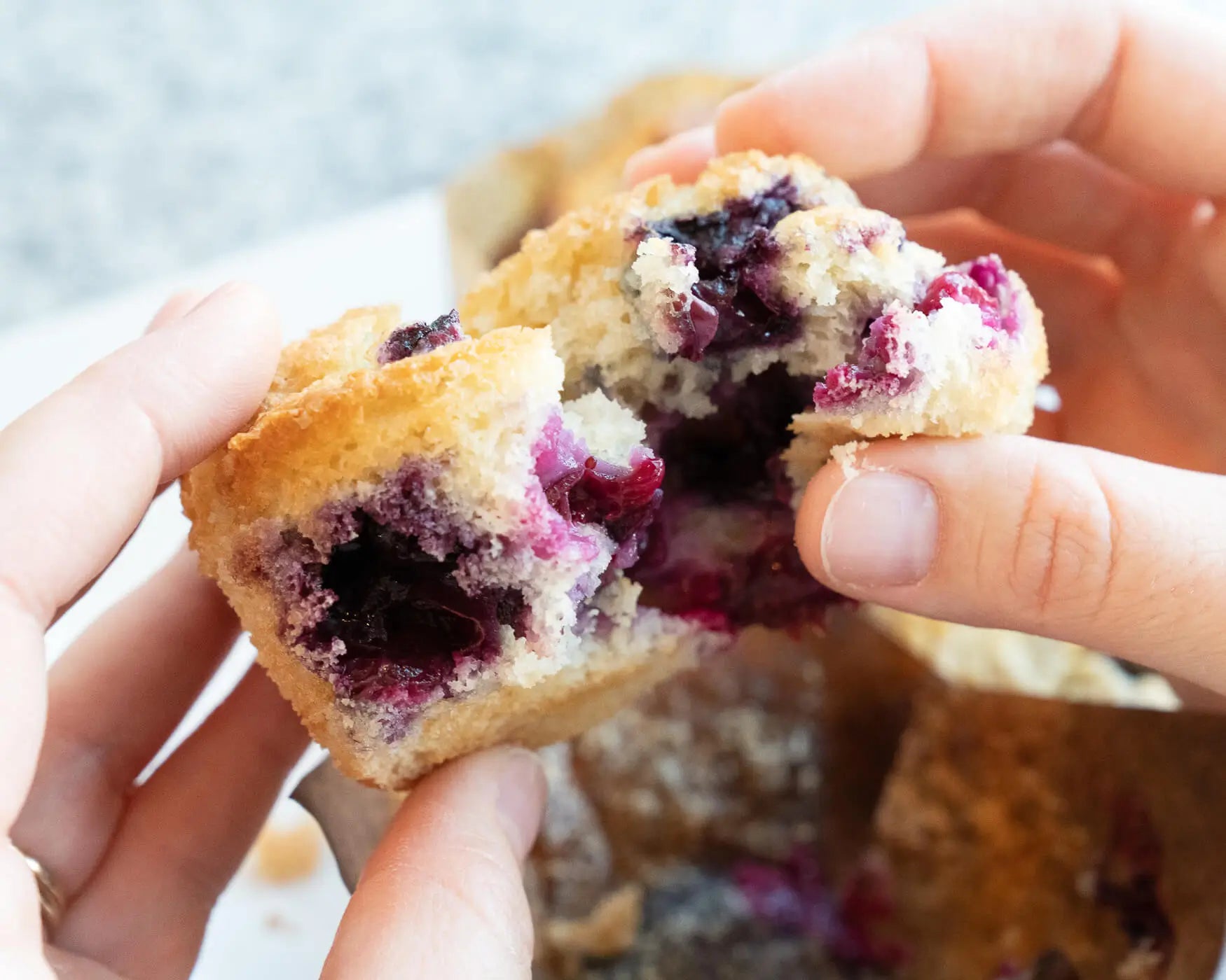 Hands breaking open a blueberry crumb muffin with fresh berries